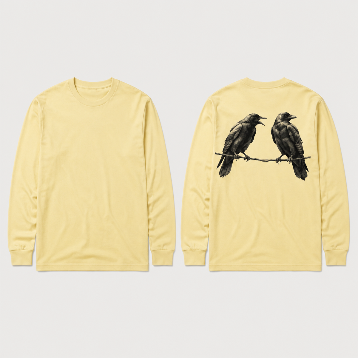 Front and back concept views of a pale-butter long-sleeve tee with one crow calling toward a second crow looking away, both perched on a thin line across the upper back.