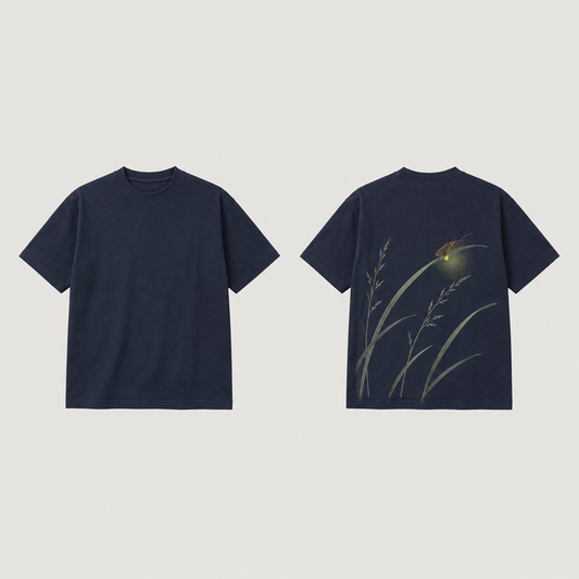 Front and back of a night-navy tee; pale arching grasses and a small firefly with a painted yellow-green glow appear on the back, with a plain front.